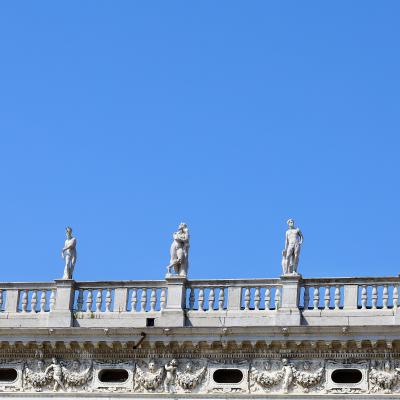 Witte standbeelden op een balustrade tegen een blauwe lucht.