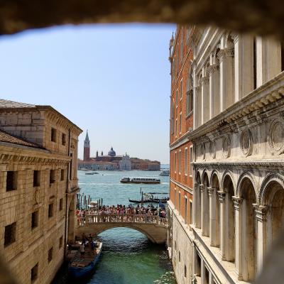 Uitzicht door een boog op een kanaal in Venetië met een brug en historische gebouwen. In de verte zie je de San Giorgio Maggiore kerk.
