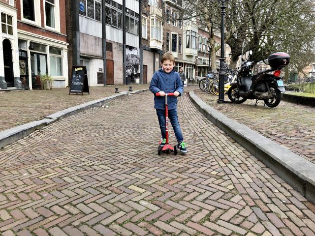 Jongen op een step over een straat met klinkers
