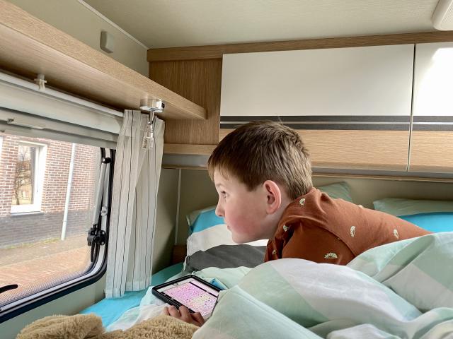 jongen kijkt door een raam van de camper naar buiten