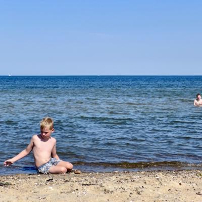 Mats in de zon op het strand, met Hugo op de achtergrond in zee