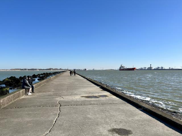 de pier van Hoek van Holland richting kust, met links het strand en rechts de Nieuwe Waterweg met een groot vrachtschip