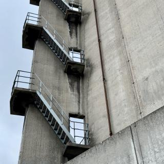 Een betonnen toren met een zigzag trap en metalen railingen, onder een grijze hemel.