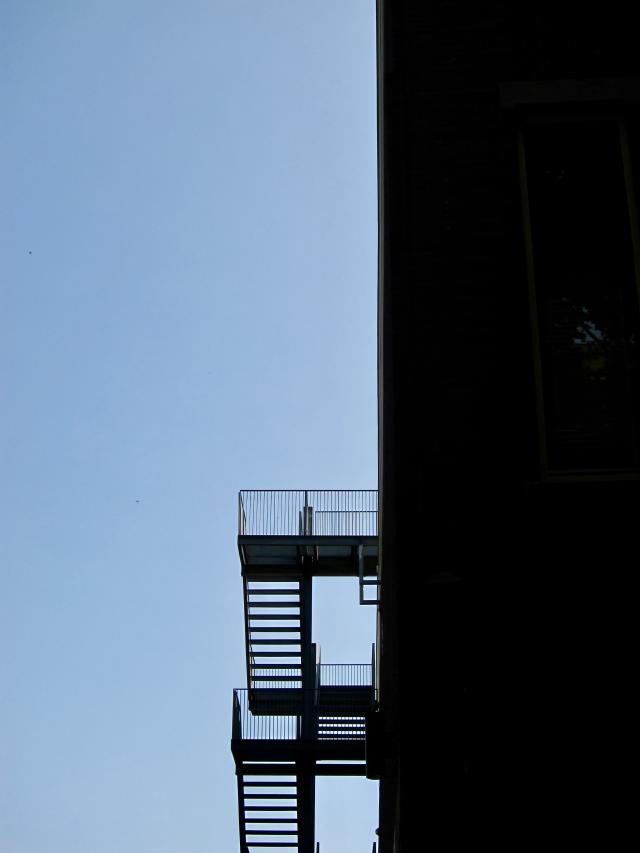 Donkere gebouw met open trappen tegen een blauwe lucht.